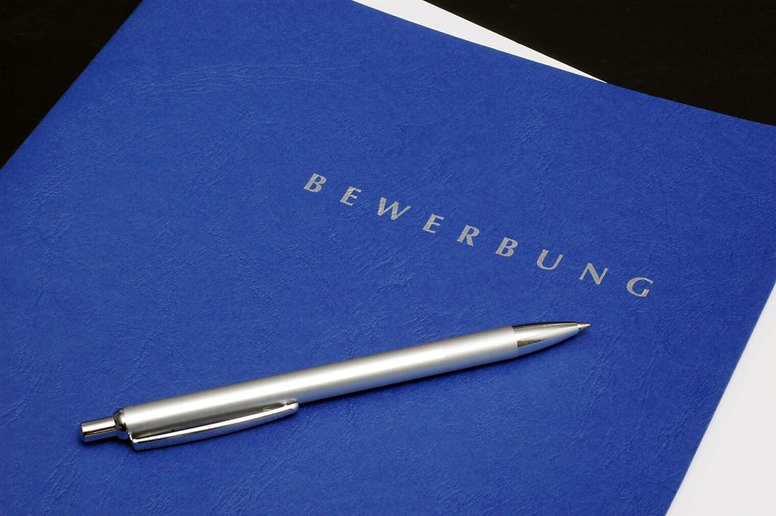 karriere, aufstieg, bewerbung, bewerbungsmappe, bewerbungsunterlagen Eine königsblaue Bewerbungsmappe mit einem Kugelschreiber darauf