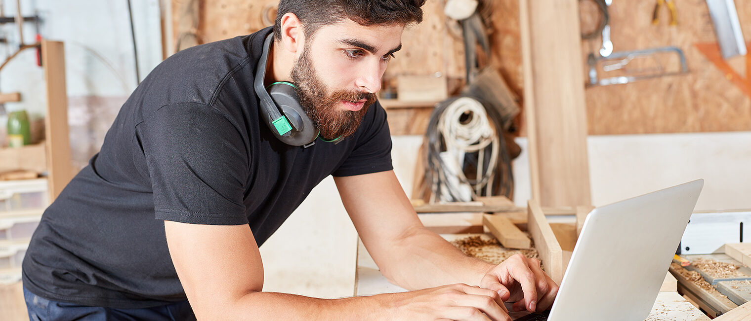 Handwerker mit Laptop in Werkstatt Handwerker mit Laptop in Werkstatt