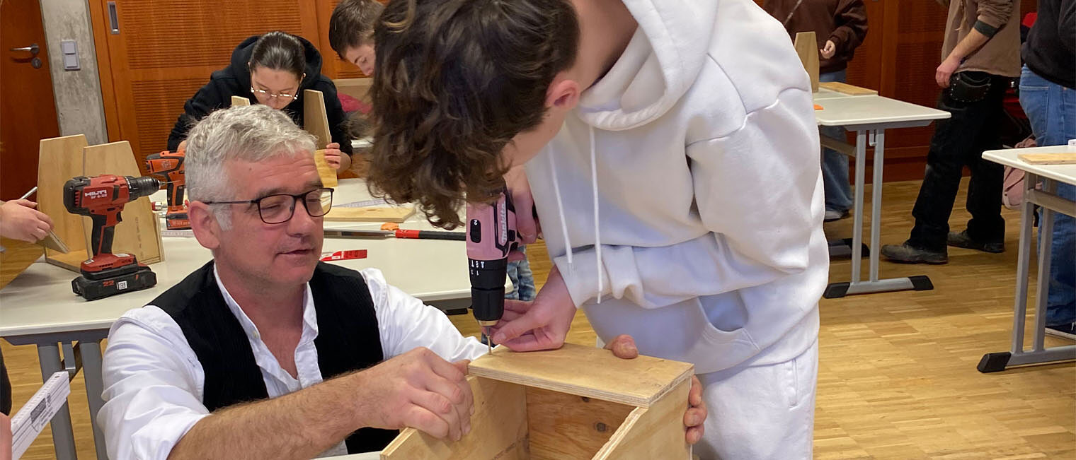 Realschule Kitzingen | Tag des Handwerks an bayerischen Schulen Zimmerer zeigt Schüler zusammenstecken einer Holzkiste