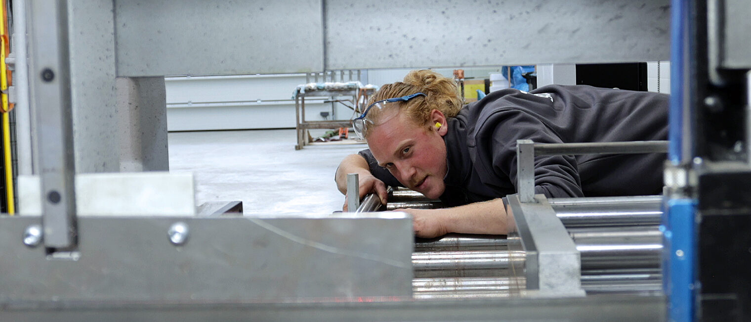 Informationen zur Ausbildungsmöglichkeiten im Handwerk Metallbauer an einer Maschine. Er schaut auf ein Metallteil.