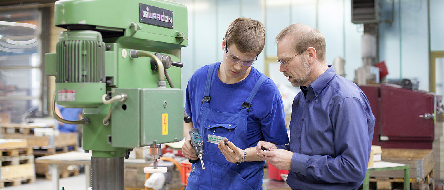 Ein Auszubildender mit Meister, in einer Werkstatt Ein Auszubildender mit seinem Meister, beide stehen in einer Werkstatt vor einer Maschine, beide tragen Schutzbrillen