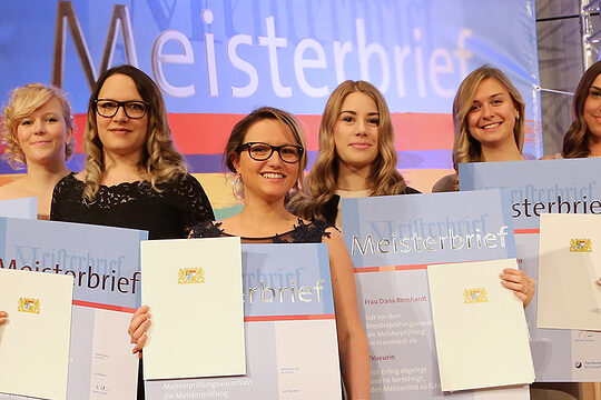 Sieben Meisterinnen im festlichen Outfit mit Meisterbriefen in der Hand, die sich über ihren Abschluss feiern. 