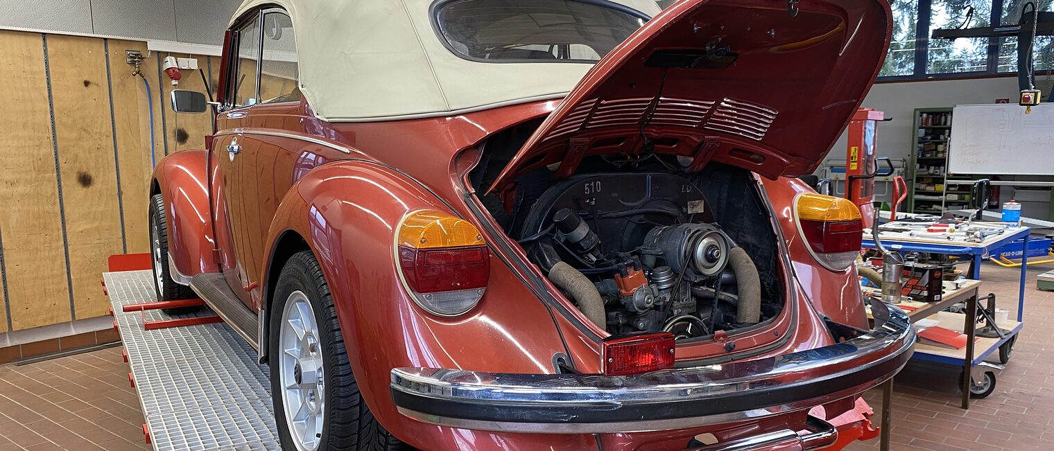 VW Käfer Ein roter VW Käfer mit offenem Motorraum steht in einer Werkstatt auf einer Hebebühne.