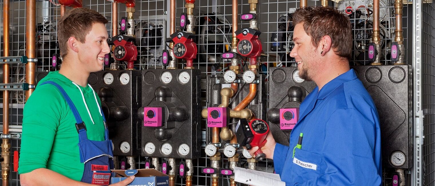 Anlagenmechaniker/-in für Sanitär-, Heizungs- und Klimatechnik Zwei Männer Anlagenmechaniker/-in für Sanitär-, Heizungs- und Klimatechnik unterhalten sich bei der Arbeit