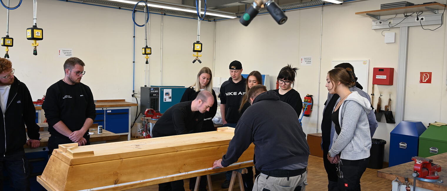 Bestatter Münnerstadt Auszubildende stehen um einen Sarg und messen ihn aus