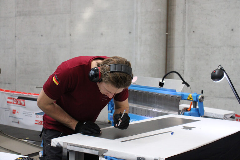 Spengler zeichnet an Blech an einer Arbeitsplatte an