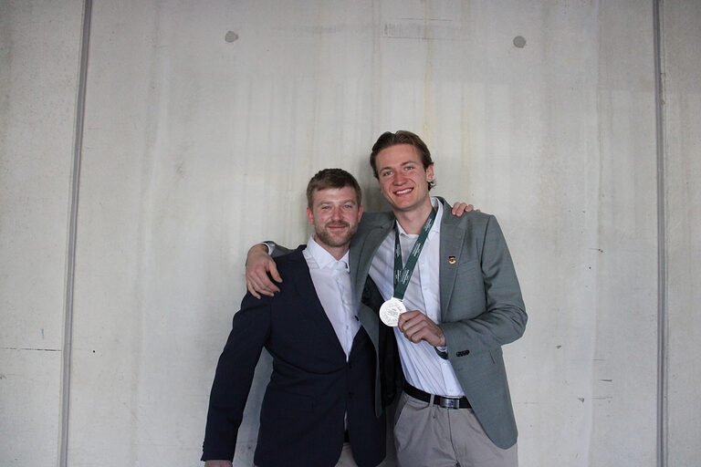 Zwei Männer halten sich im Arm und zeigen Silbermedaille in Kamera