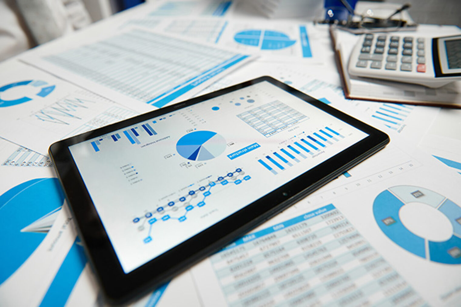 Schreibtisch mit iPad und Ausdrucken von Diagrammen und Statistiken zur Auftragskalkulation und -steuerung